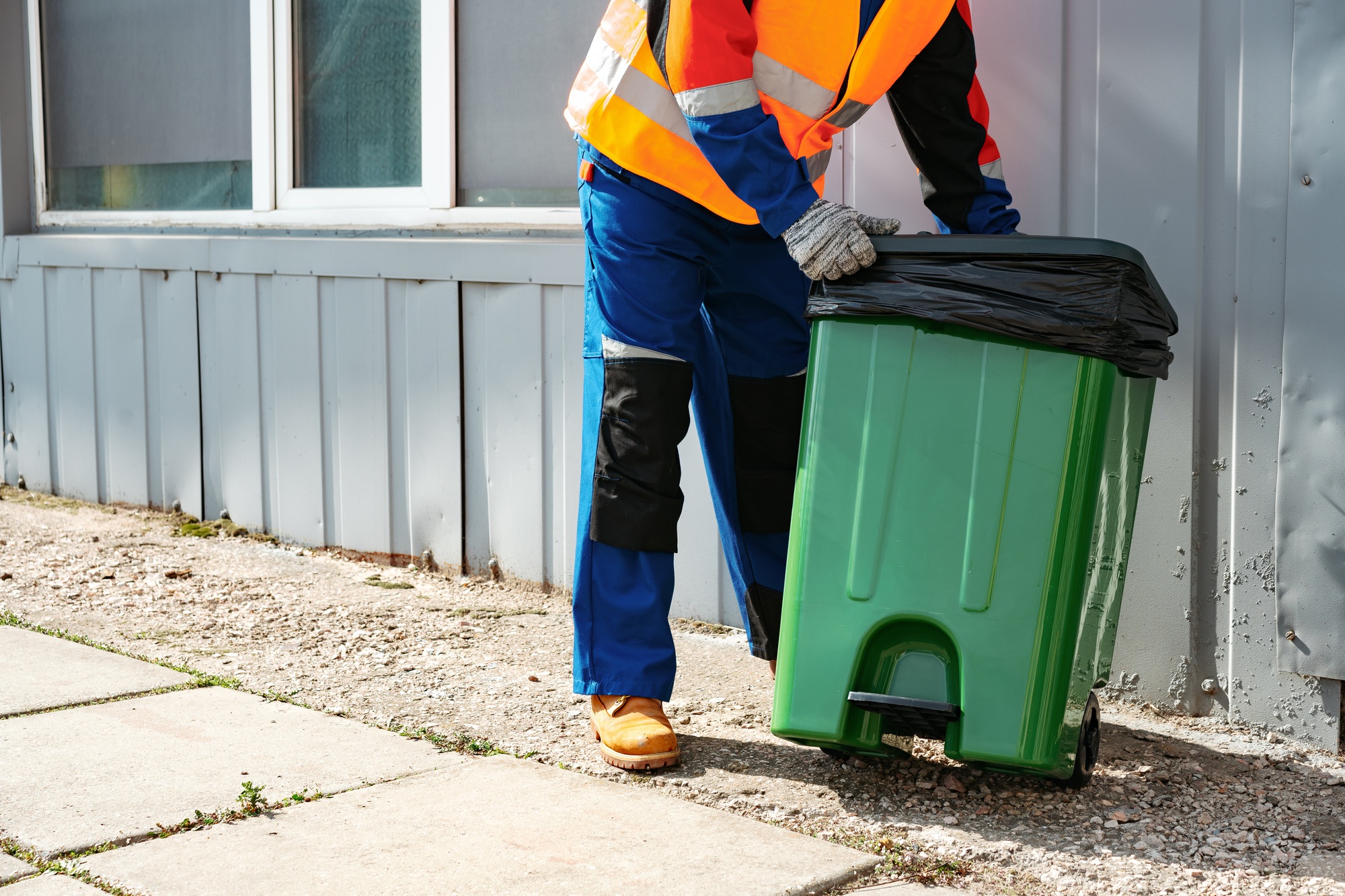 Male janitor in uniform cleans a trash can in the street